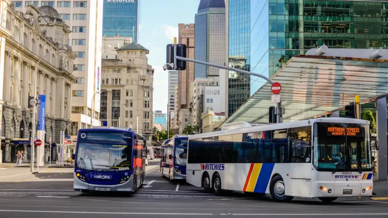 Pilsētas satiksmes autobusi brauc pa ielu lielpilsētas centrā dienas gaismā.