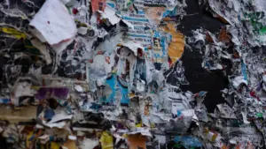 Nolietots sludinājumu dēlis ar saplēstiem papīriem, simbolizējot nepieciešamību pēc mājas ārējās apkopes un remonta.