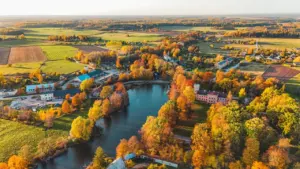 Rudens ainava ar upi un krāsainiem kokiem Latvijas mazpilsētā no augšas.