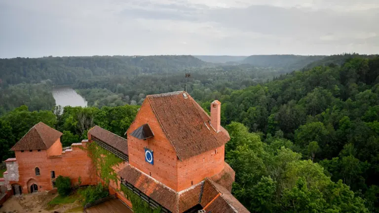 Turaidas pils majestātiskais skats Siguldā, ieskauts zaļā mežā un Latvijas dabas ainavā.
