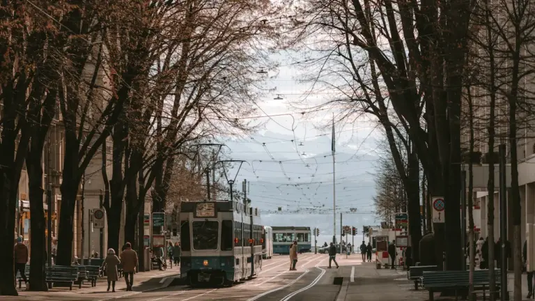 Cilvēku pilna Cīrihes iela ar tramvaju, kokiem un skaistu pilsētas noskaņu rudenī.
