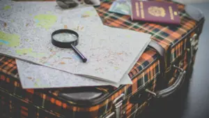 Vecmodīgs koferis ar karti un palielināmo stiklu, kas simbolizē ceļu uz nezināmo.